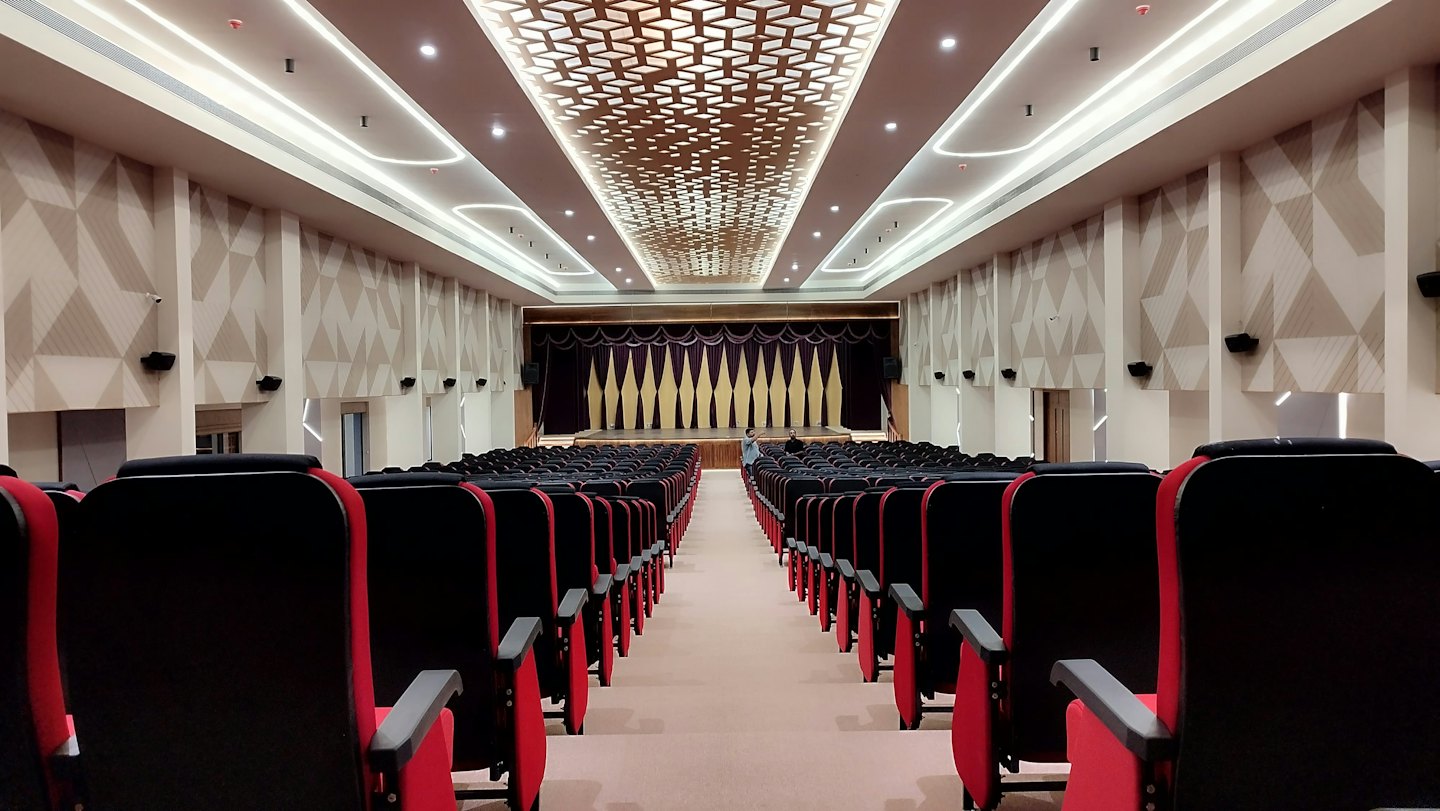 Posti vuoti in un auditorium di fronte a un palco con tende viola e oro.
